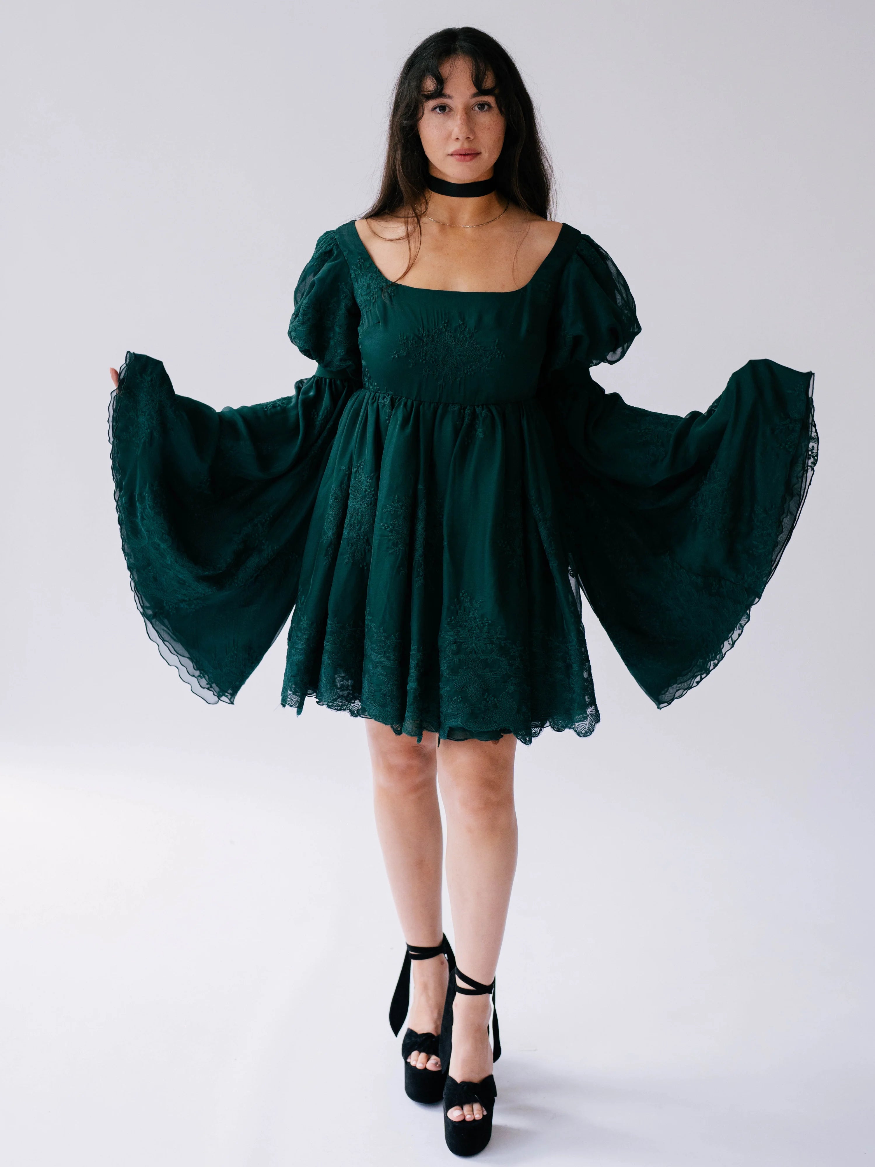 Dark emerald green mini dress with dramatic bell sleeves and lace trim.