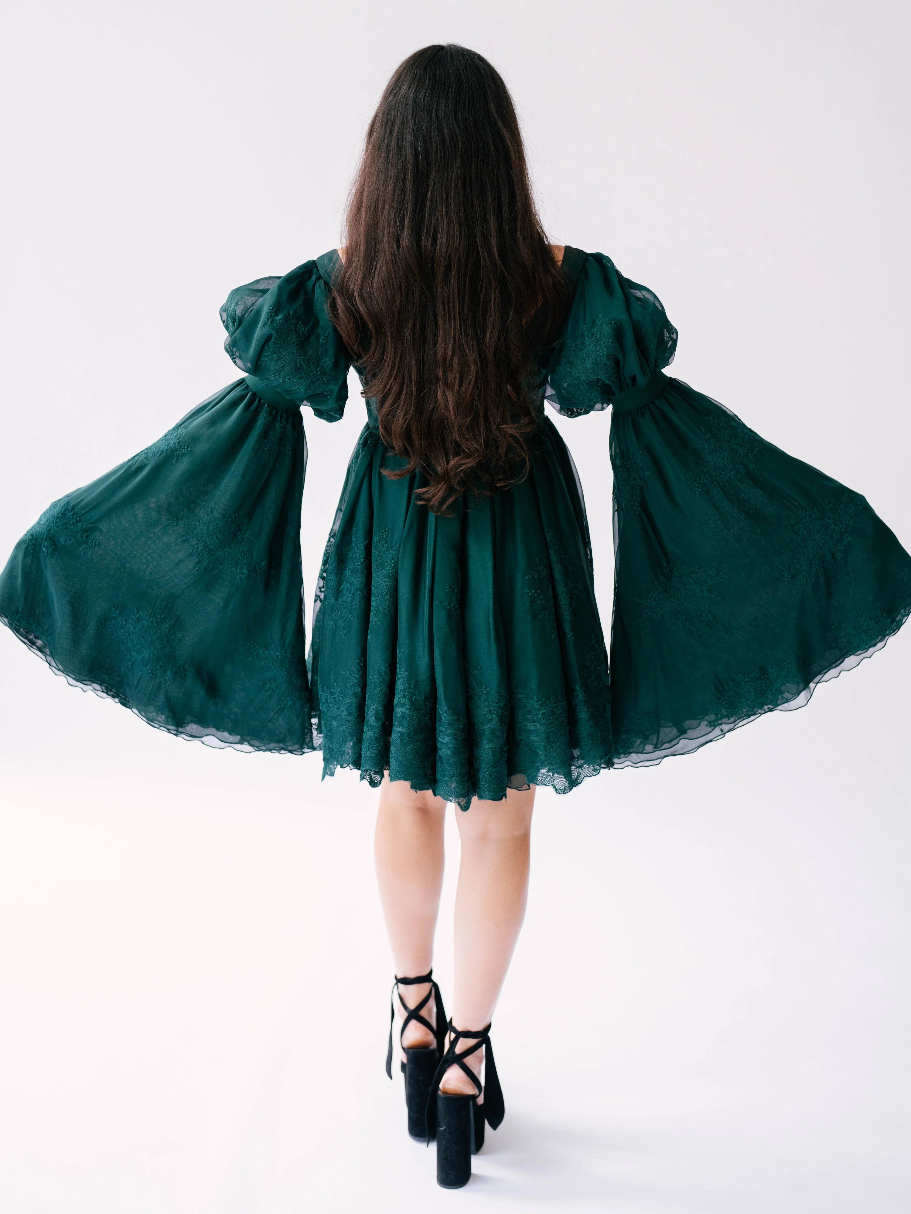 Emerald green holiday mini dress with puff sleeves and lace trim worn with black strappy heels.