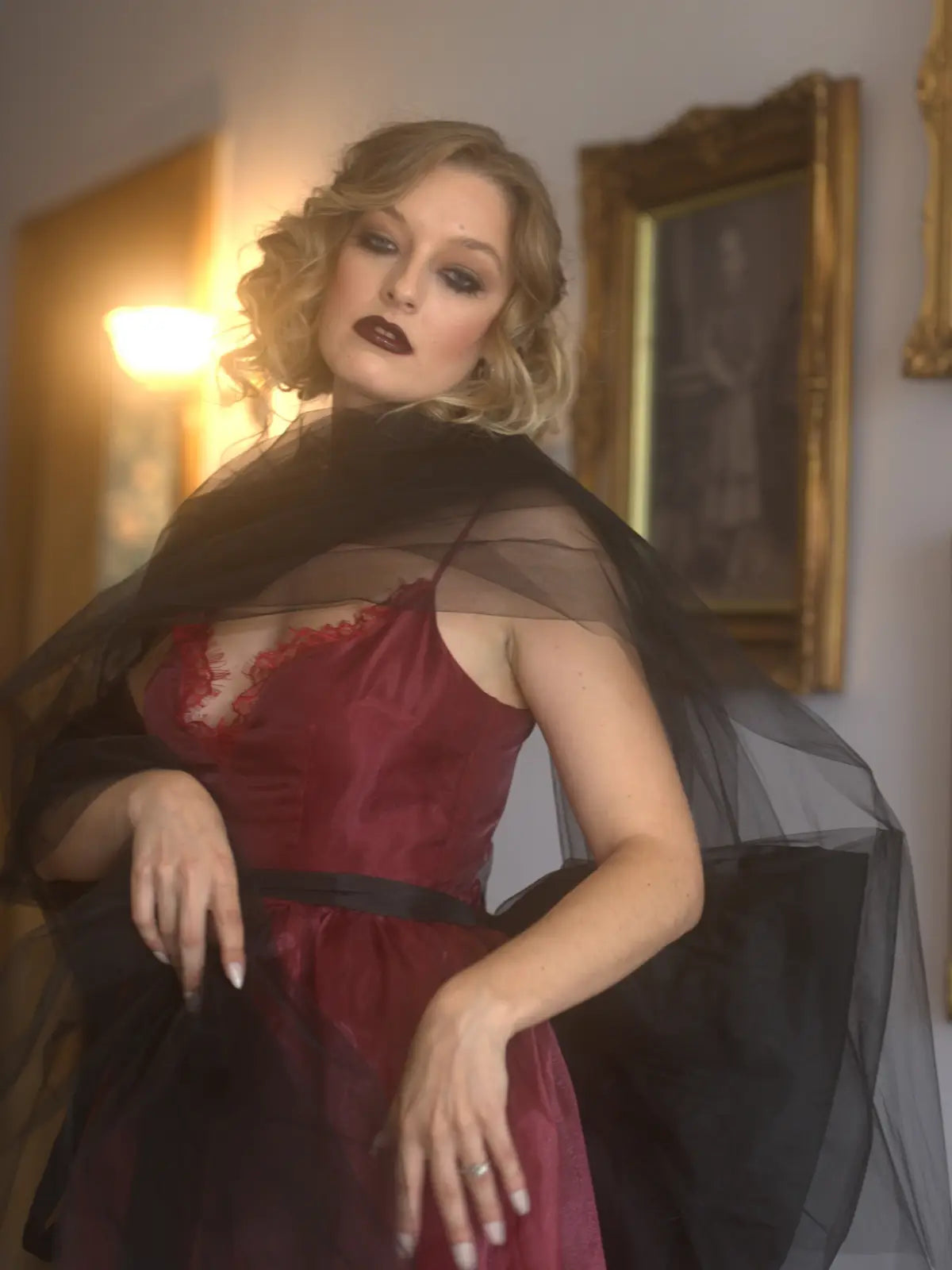 A woman in a red organza maxi dress with a black organza bow in an ornate room with paintings on the wall.