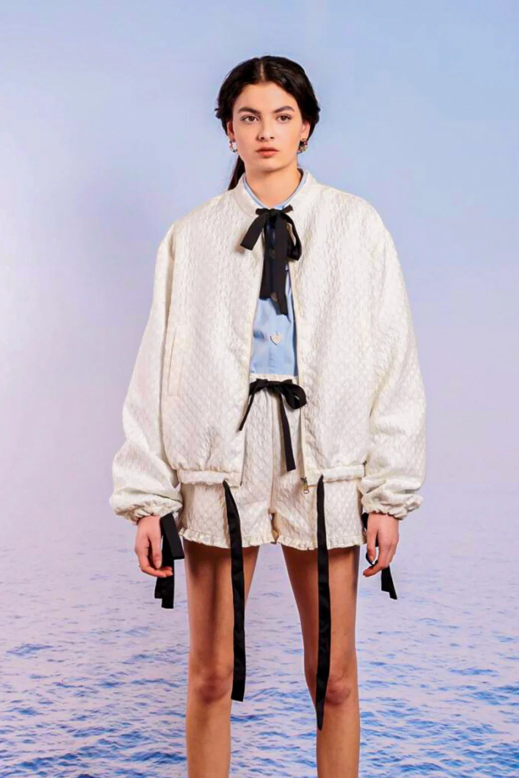 Woman in a white Adella Jacquard Bomber Jacket styled with shorts and a black bow tie