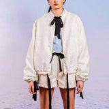 Woman in a white Adella Jacquard Bomber Jacket styled with shorts and a black bow tie