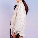 Woman in white oversized cardigan with black bows, featuring Adella Jacquard Bomber details