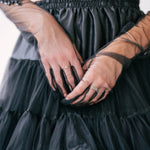 Woman wearing a black tulle skirt and sheer formal evening gloves with visible rings.