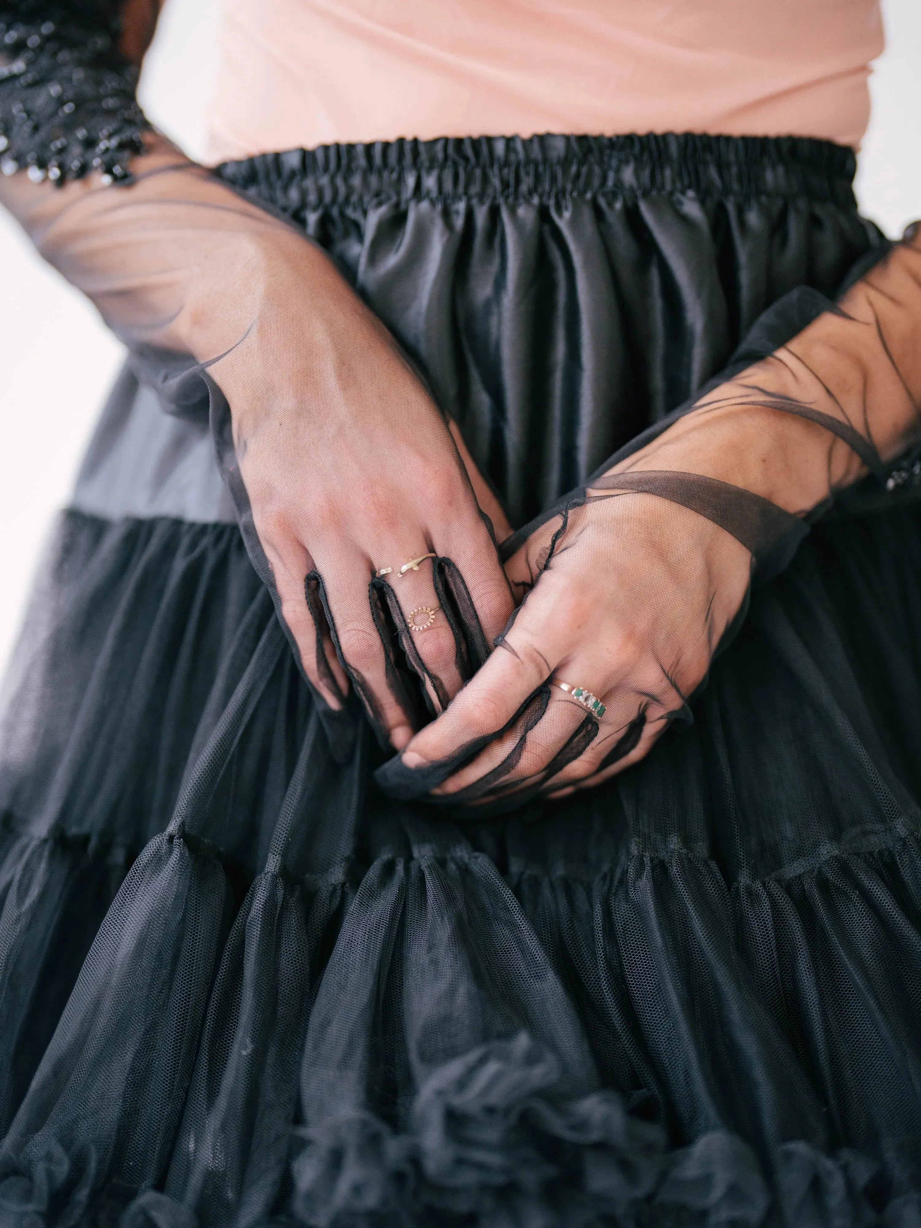 Woman wearing a black tulle skirt and sheer formal evening gloves with visible rings.
