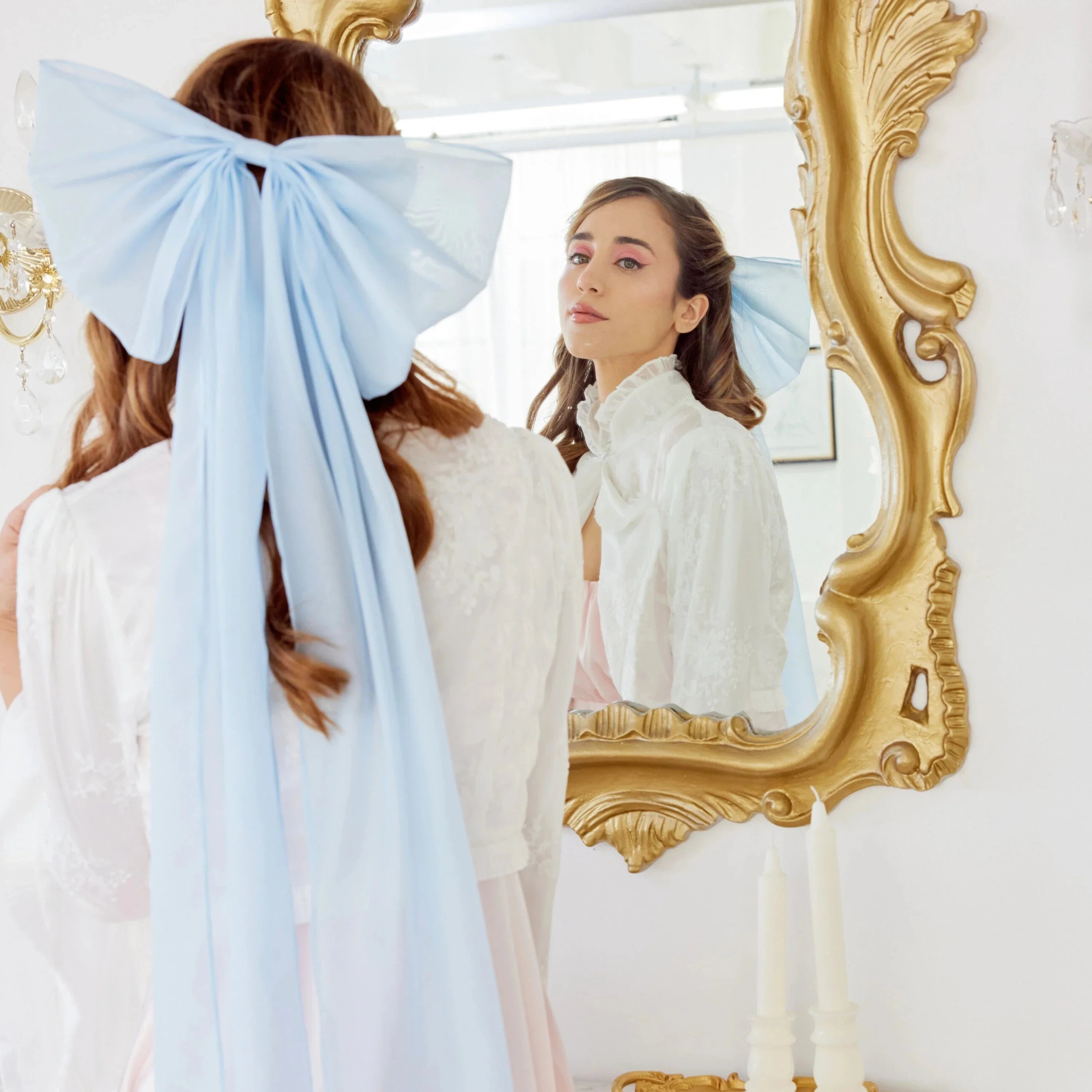 Ornate gold-framed mirror reflecting woman in white dress and light blue Giant Flutter Bow