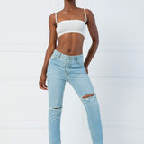 Woman in light blue ripped jeans and white crop top featuring the Atwood Camisole design