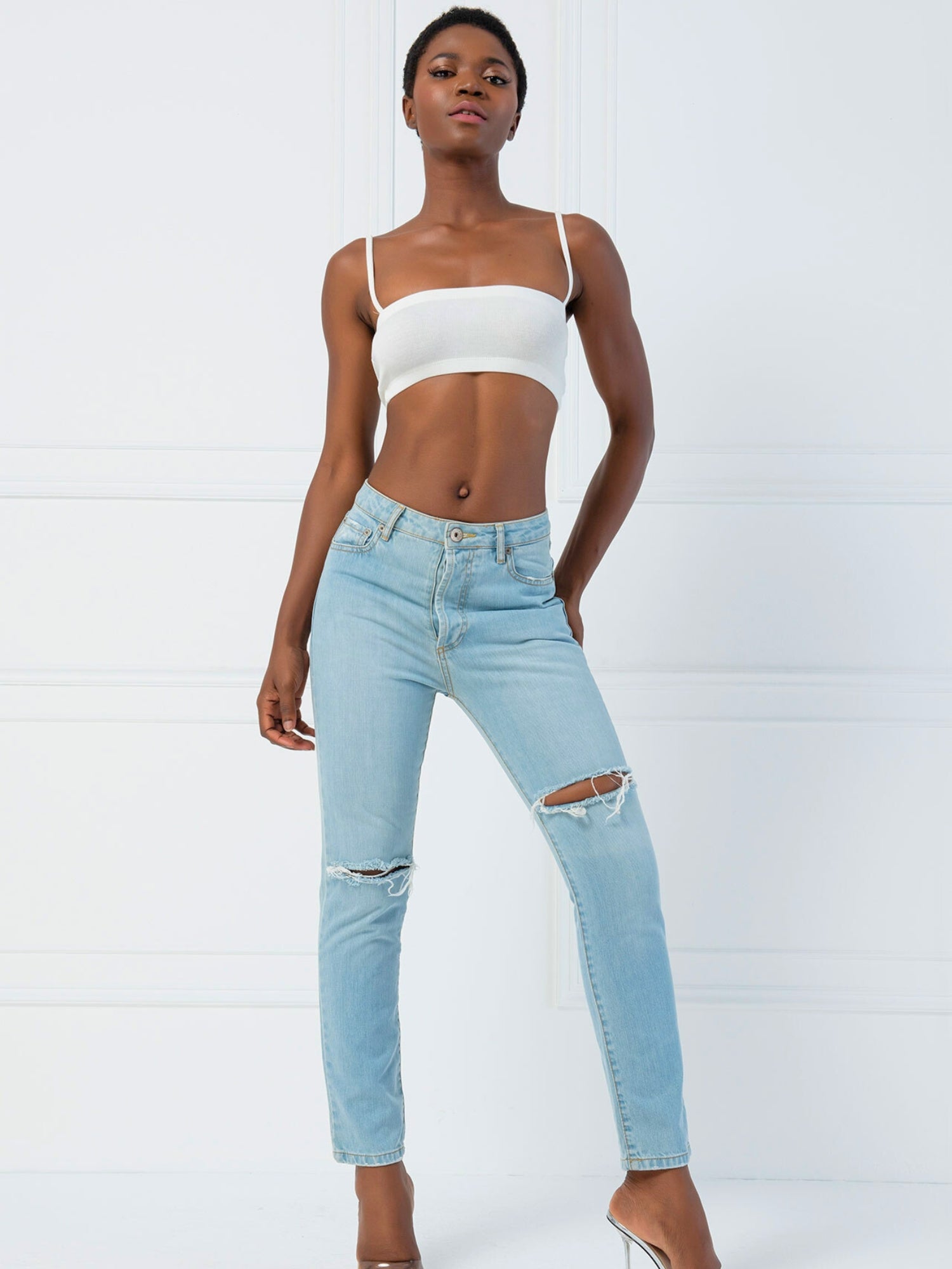 Woman in light blue ripped jeans and white crop top featuring the Atwood Camisole design