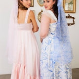 Two women in elegant pink and blue floral dresses with a giant flutter bow