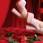 Barbie’s Pink Penny Loafers elevated on legs against a red backdrop, highlighting the glossy pink platform design and block heel silhouette.