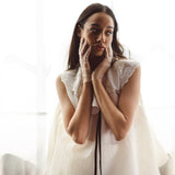 Woman in a white gown with hands near her face, showcasing the Beaded Botanic Top