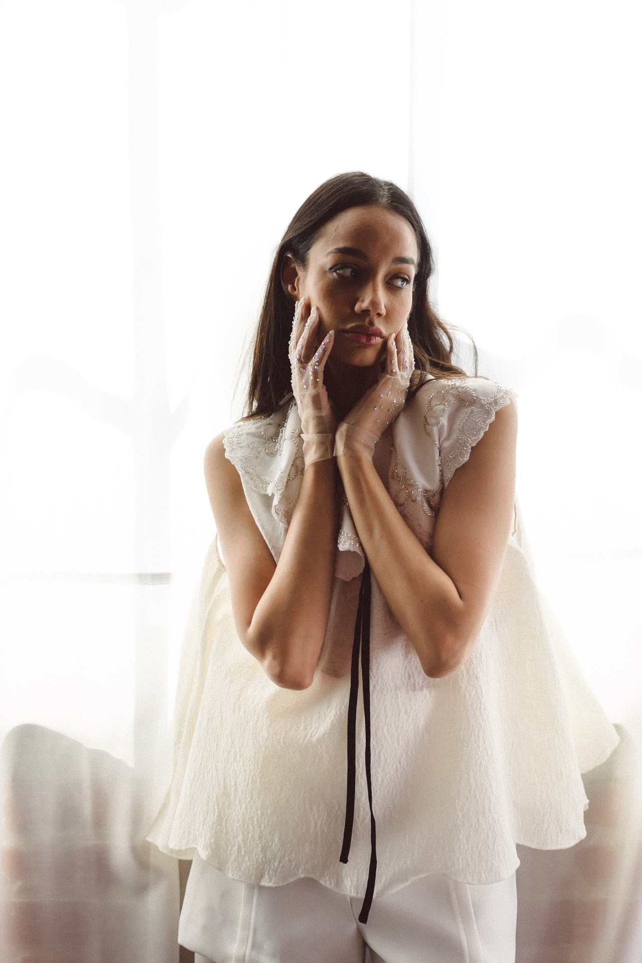 Woman in a white gown with hands near her face, showcasing the Beaded Botanic Top