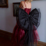 A woman wearing the Harlow organza midi dress with the black swan grand bow sash in an elegant room.