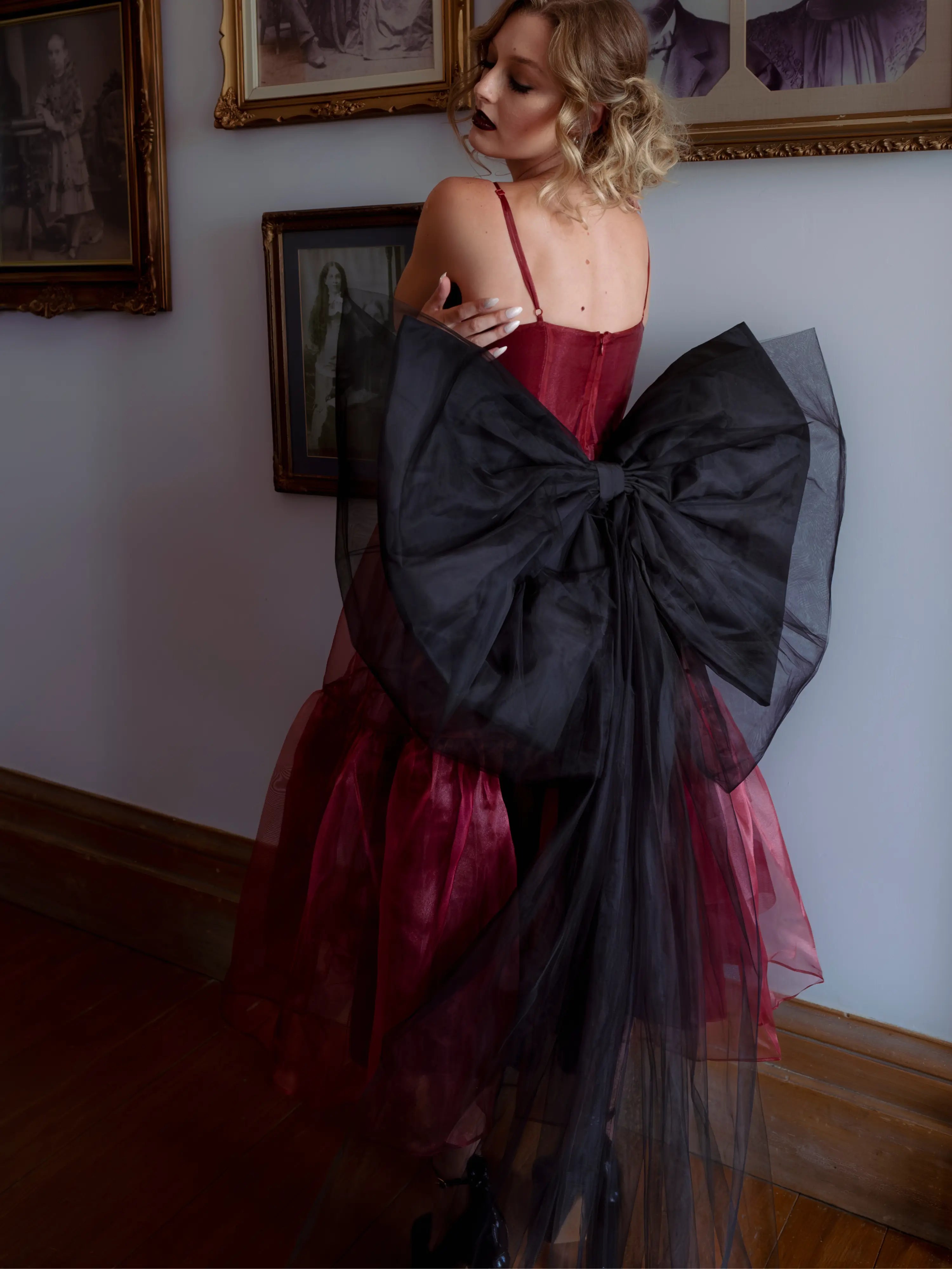 A woman wearing the Harlow organza midi dress with the black swan grand bow sash in an elegant room.