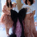 The Black Swan Grand Bow Belt adds bold elegance to a whimsical group look, paired with floral dresses and pastel tones in a fairytale setting.