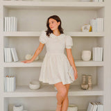 Woman in a short white puffed sleeve dress from Blue Blooms Lamb Mini Dress collection