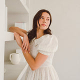 Woman in a white dress with puff sleeves posing thoughtfully in Blue Blooms Lamb Mini Dress