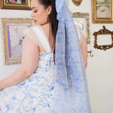 A woman wearing a white dress with a blue toile hair bow in an ornate room.