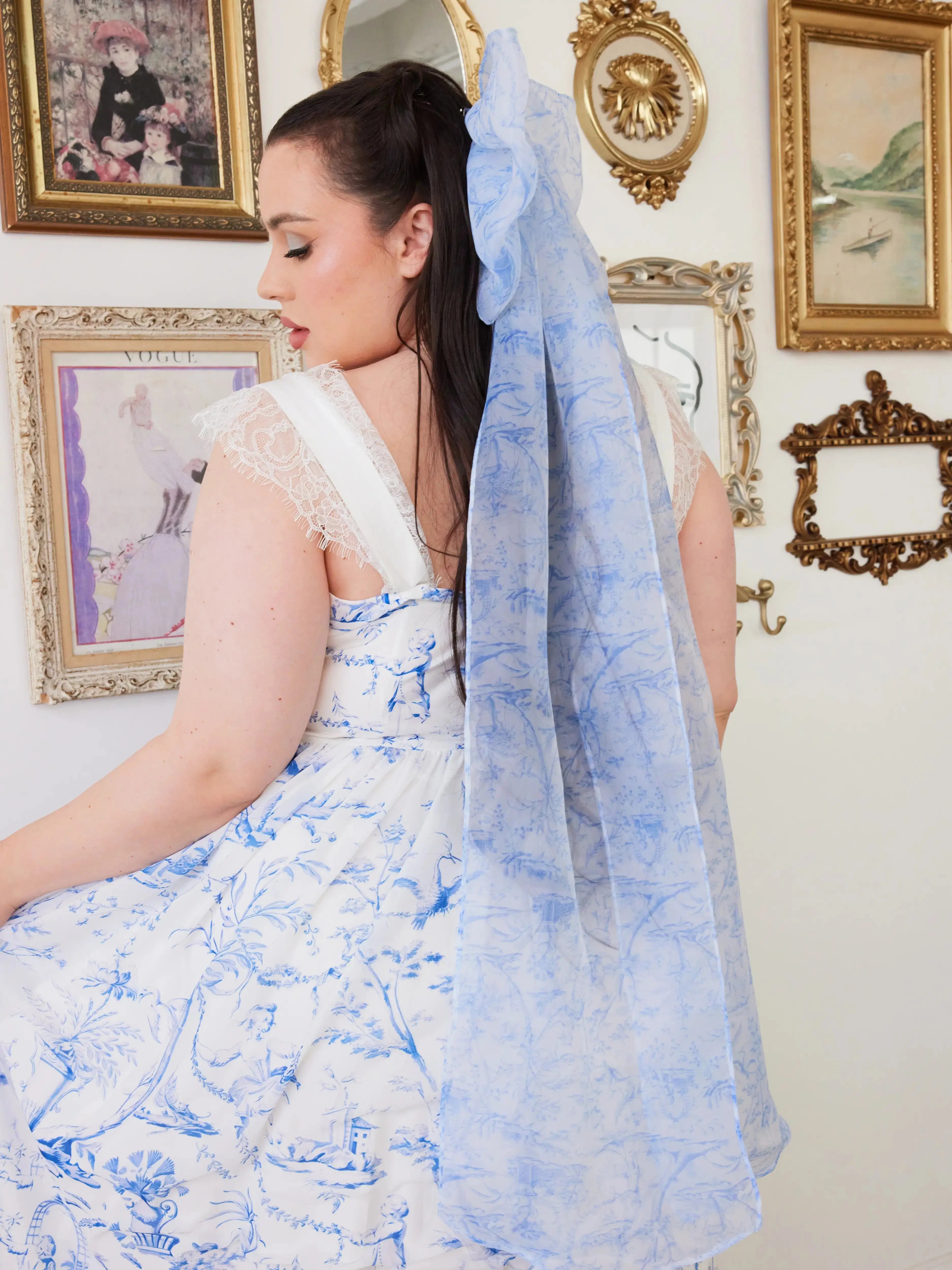 A woman wearing a white dress with a blue toile hair bow in an ornate room.