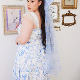 A woman wearing a white maxi dress with a blue toile hair bow in an ornate room.