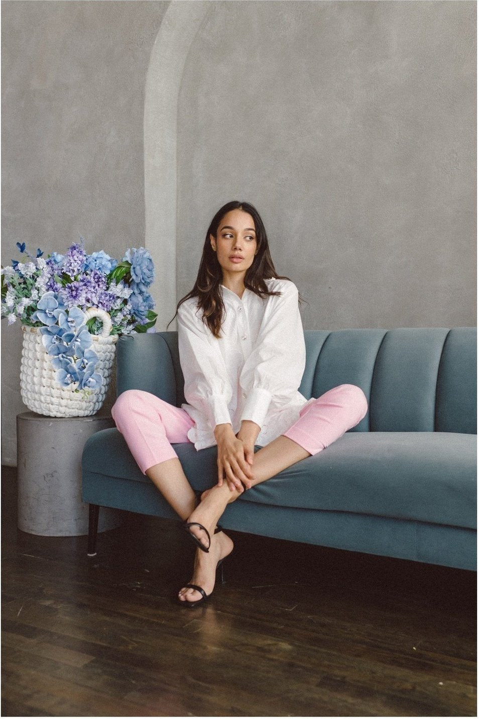 Woman in a white broidered botany shirt and pink pants sitting on a teal couch