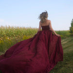 A woman wearing the Cathedral Crimson Red Lace Dress is running in a field with a clear sky.