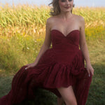 A woman wearing the Cathedral Crimson Red Lace Dress is walking in a grassy field.