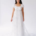 A floor-length white empire waist lace gown with short puff sleeves and delicate star and moon details.