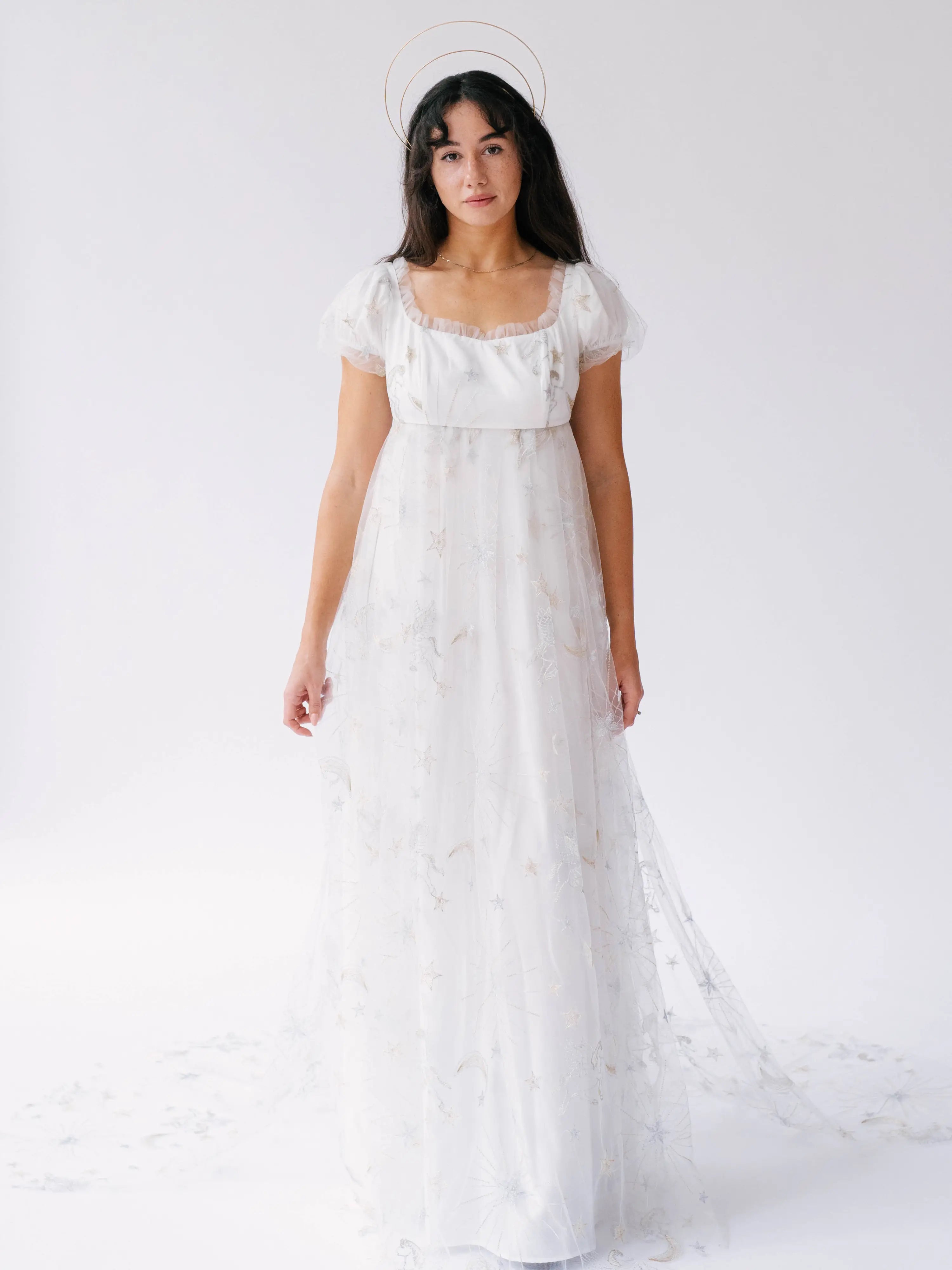 A floor-length white empire waist lace gown with short puff sleeves and delicate star and moon details.