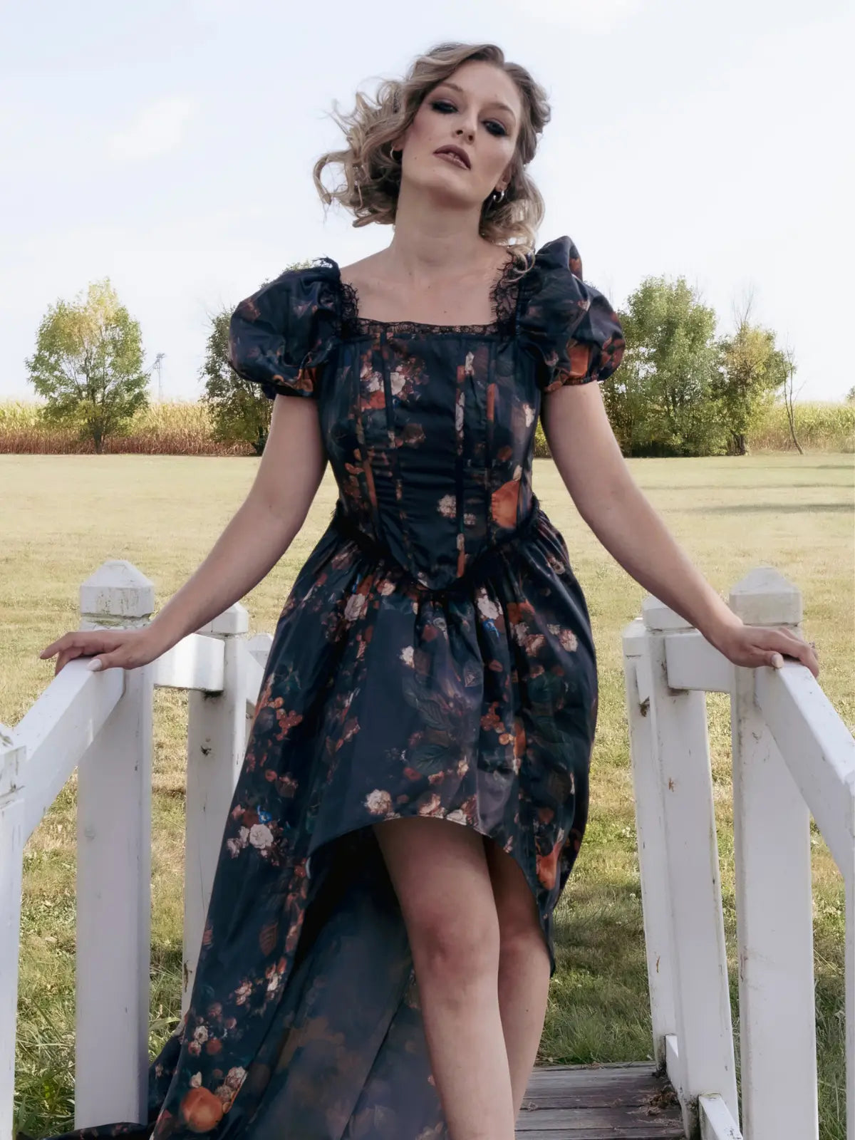 A woman in a cotton maxi dress featuring an autumn print is standing on a white wooden bridge in a field.