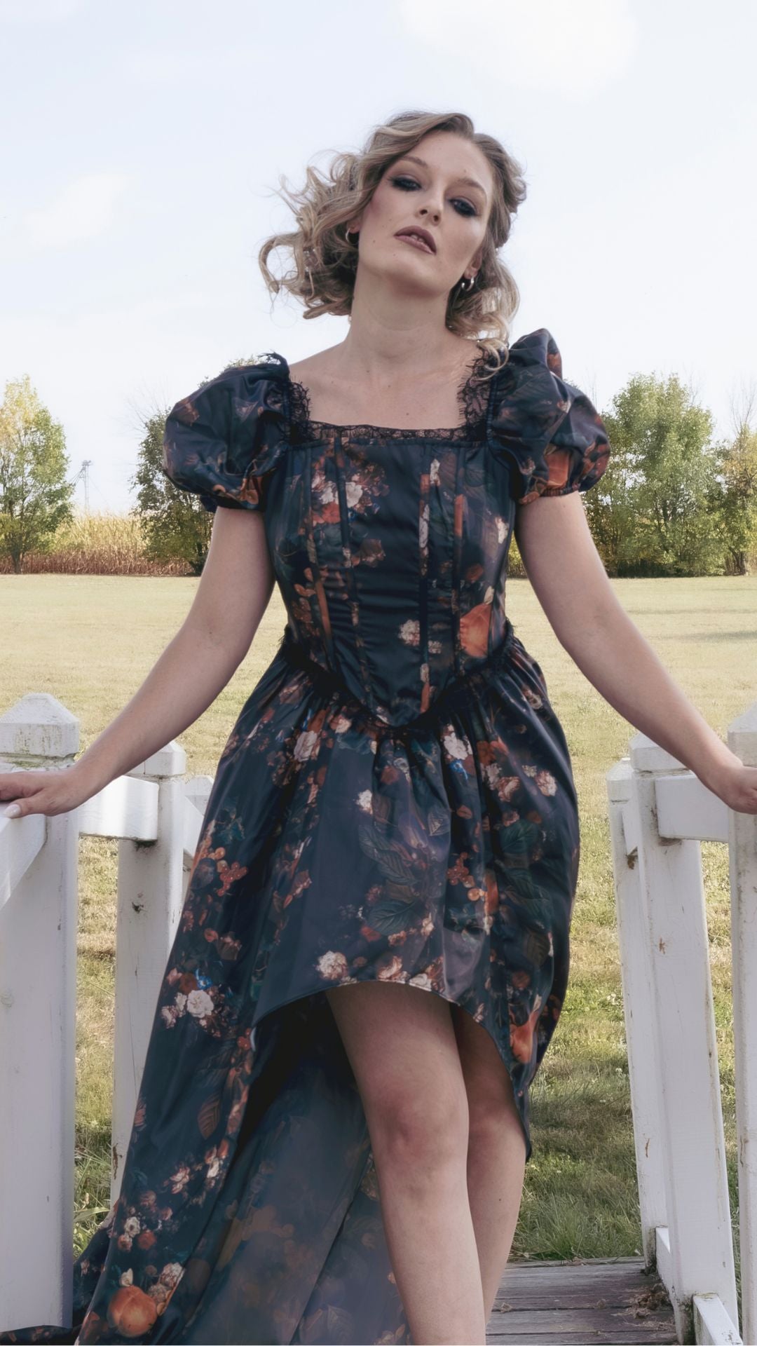 A woman in a cotton maxi dress featuring an autumn print is standing on a white wooden bridge in a field.