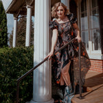 A woman wearing an autumn printed taffeta dress, standing on a porch with columns and a railing.