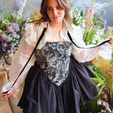 Woman in The Ciela Shrug Top featuring a black and white floral gown with lace trim