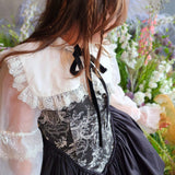 Close up view of a woman wearing a white shrug over a black corset dress in a floral setting.