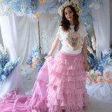 Front view of a woman wearing a t-shirt and a pink ruffle skirt in front of blue floral decorations.