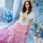 A woman wearing the dahlia pink ruffle skirt styled with a floral crown and kitten tee, highlighting the dramatic pink train and layered ruffles.