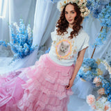 A woman wearing the dahlia pink ruffle skirt styled with a floral crown and kitten tee, highlighting the dramatic pink train and layered ruffles.