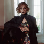 A woman wearing a stained glass satin mini dress and a dark coat in an elegant room.
