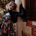 A woman wearing the Stained Rose Darling Dress, leaning against a brick wall with a window.