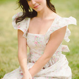 Woman in a white floral dress outdoors, showcasing the Dream Rainbow Apron Maxi