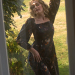 A woman in a floral cotton maxi dress standing outdoors with greenery around.