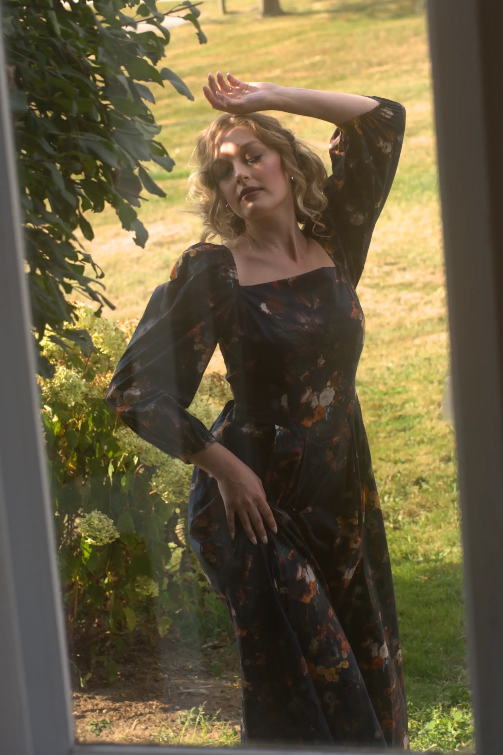A woman in a floral cotton maxi dress standing outdoors with greenery around.