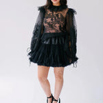 The Eleanor Midnight Black Lace Top with sheer floral lace, ruffled collar, and voluminous sleeves styled with a black mini skirt.
