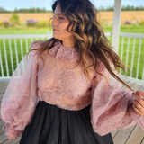 Woman in The Eleanor Top, a pink lace puff dress with voluminous sleeves and a dark skirt