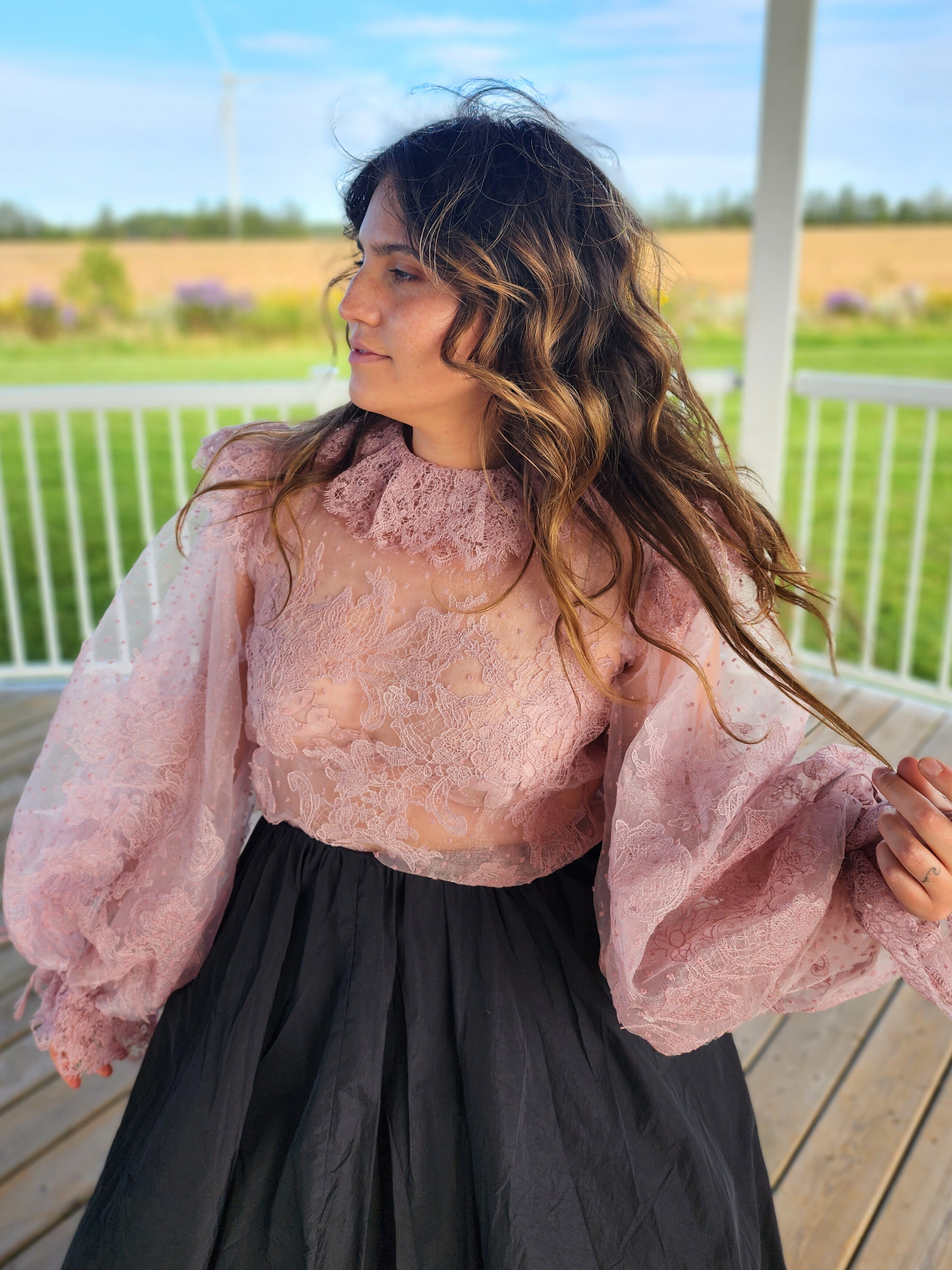 Woman in The Eleanor Top, a pink lace puff dress with voluminous sleeves and a dark skirt