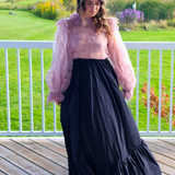 Woman in a pink top and long black skirt showcasing The Eleanor Top’s elegant style