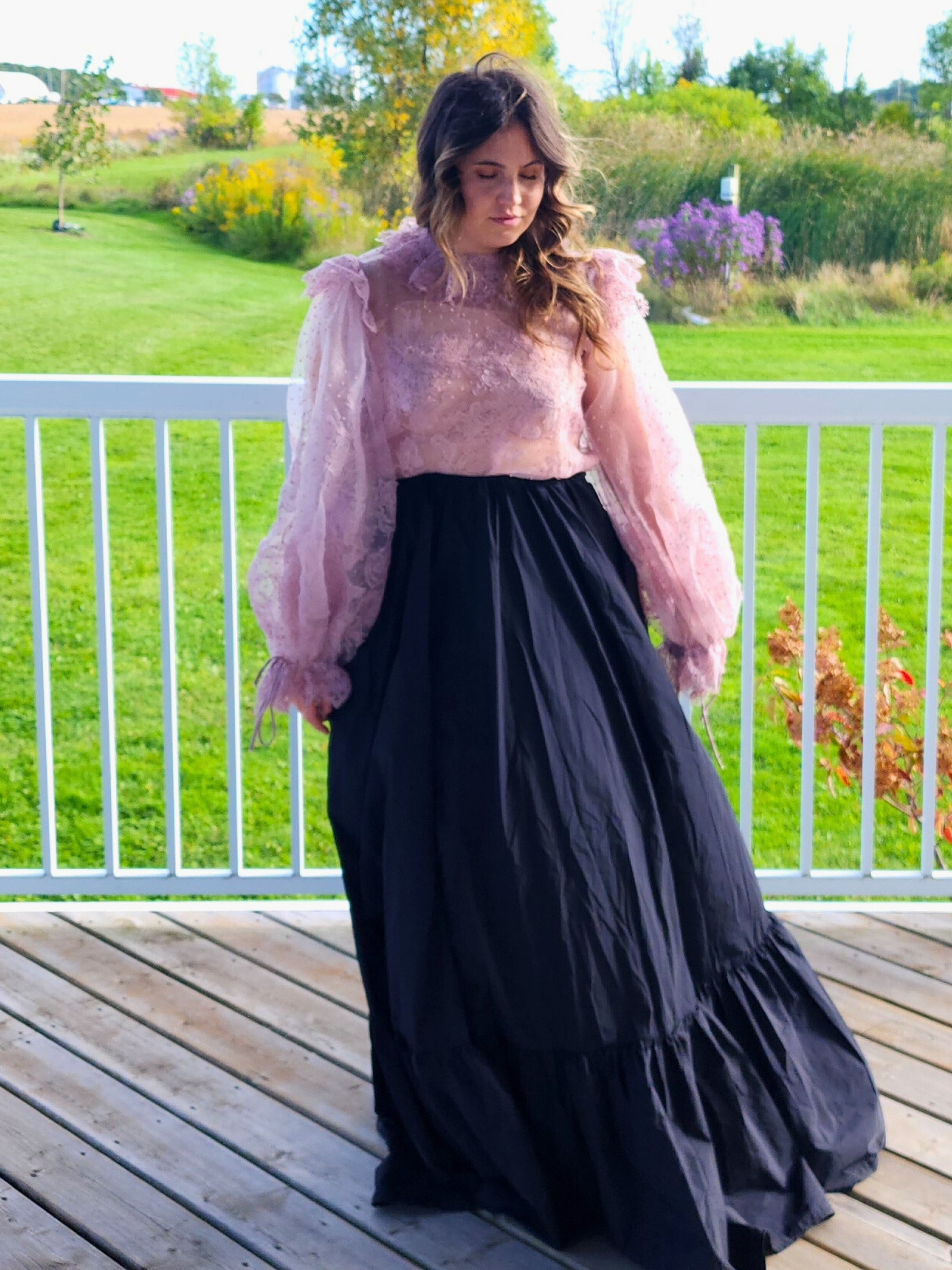 Woman in a pink top and long black skirt showcasing The Eleanor Top’s elegant style