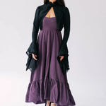 A woman wearing a black bolero jacket over a purple midi dress on a white background