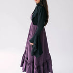 Side view of A woman wearing a black lace bolero jacket and purple midi dress against a white background.