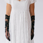 White lace dress with black lace opera gloves on a plain background