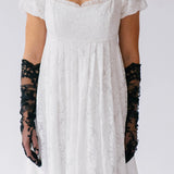 White lace dress with black lace opera gloves on a plain background
